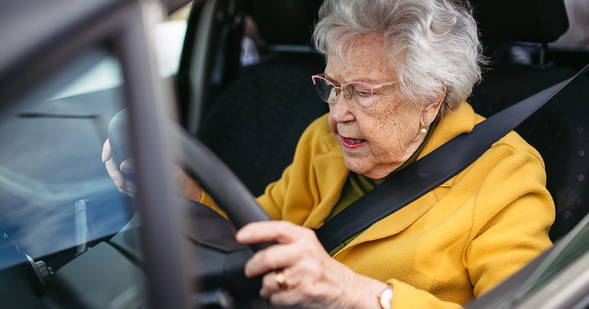 Focused senior woman driving car alone, holding steering wheel firmly. Safe driving for elderly adults, older driver safety.